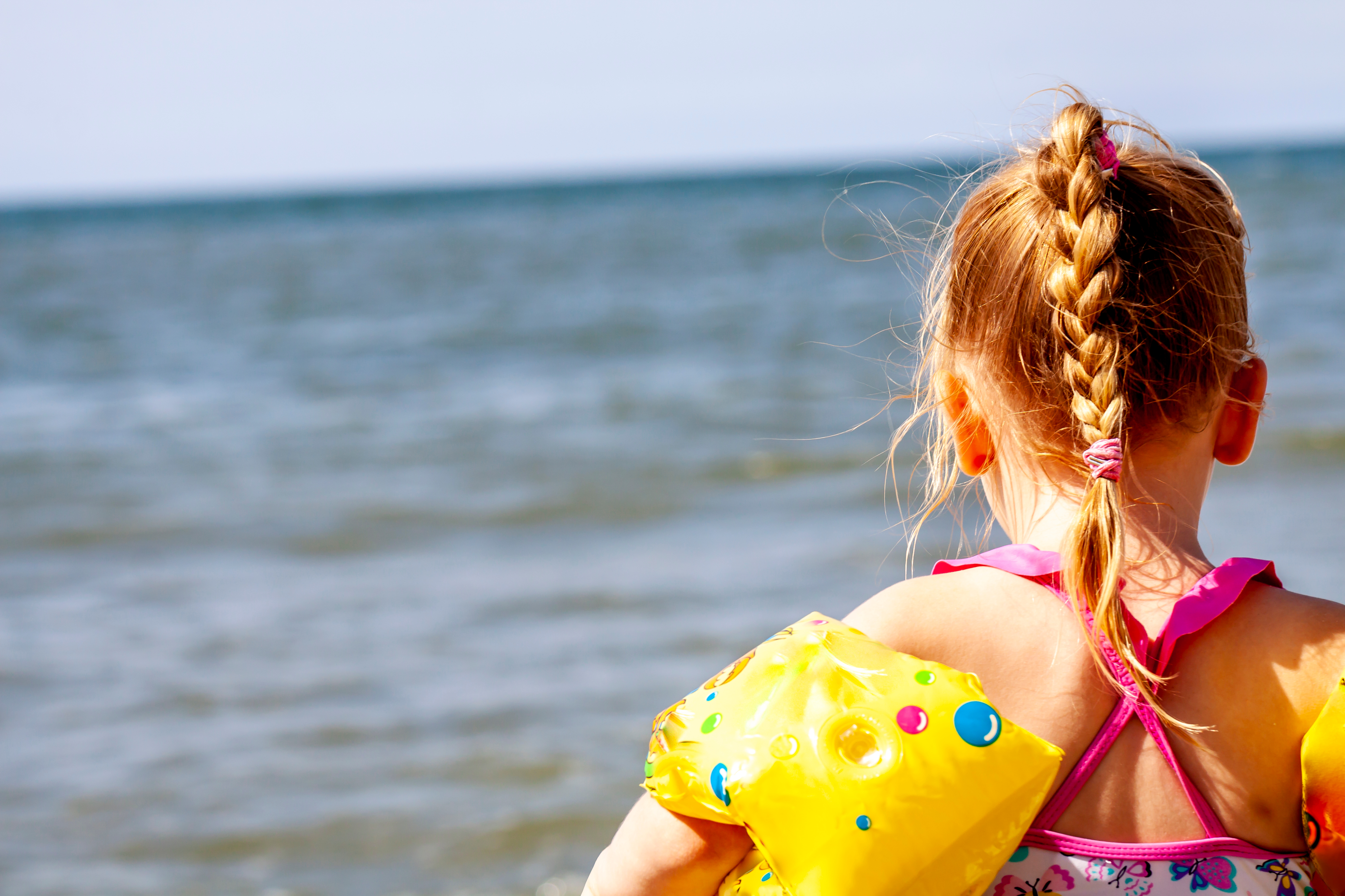 Little girl with floaties preparing to swim in the ocean.