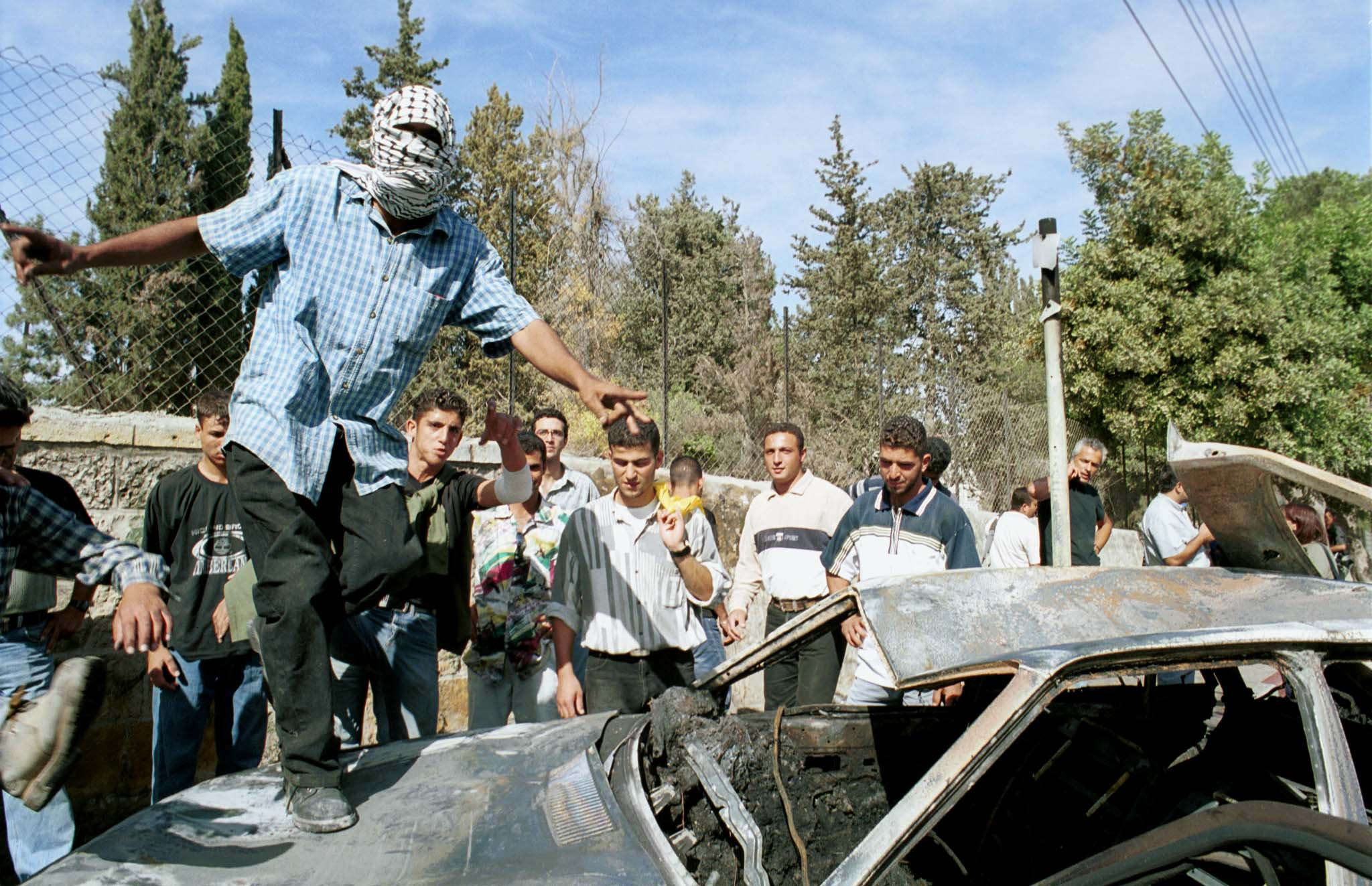  A Palestinian celebrates on top of the burned car of the two Israeli soldiers who were taken from it and lynched next to Ramallah, October 12, 2000. 