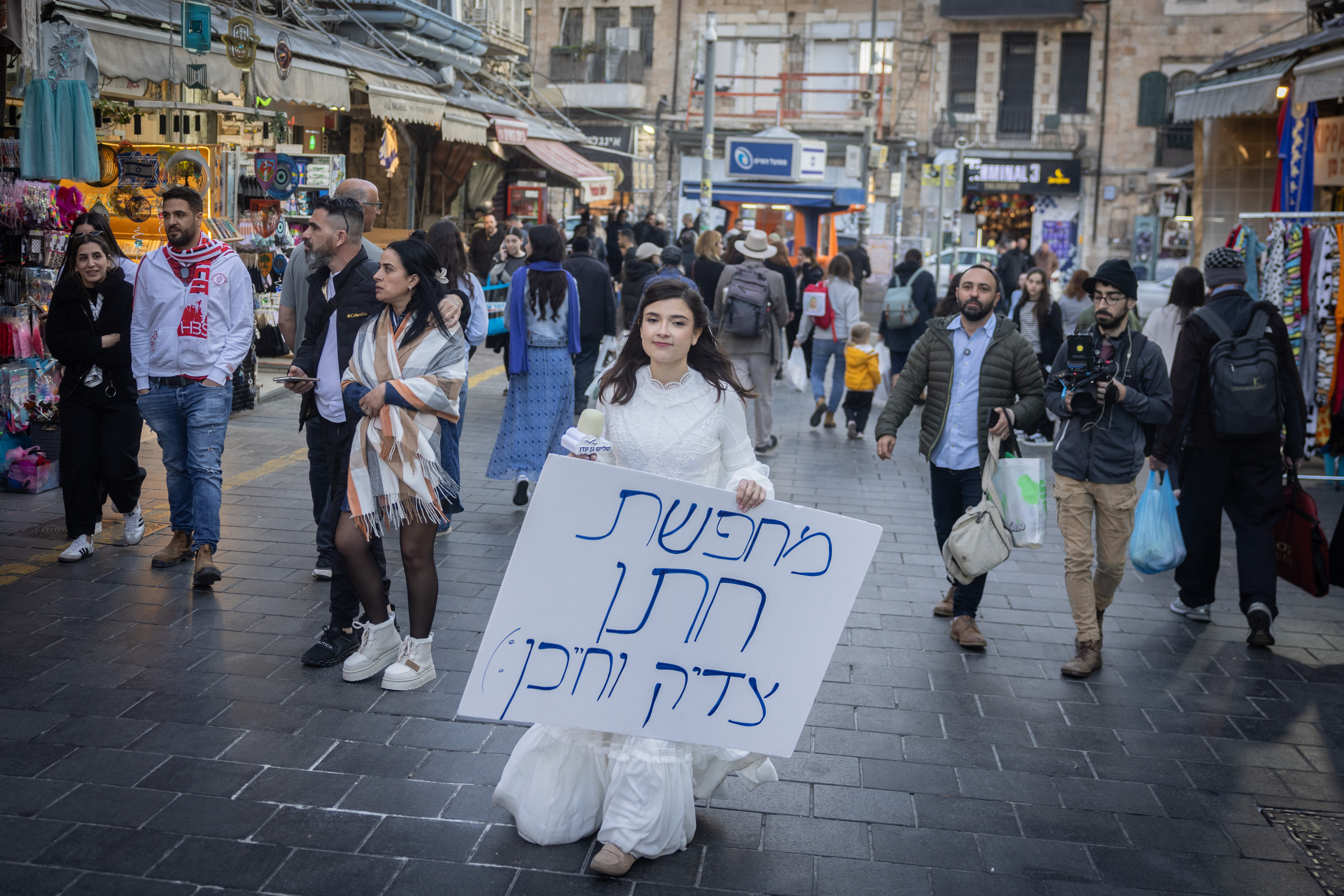  A young girl dressed up as a bride holding a sign reading "Looking for a righteous and smart groom", walks the Mahane Yehuda market in Jerusalem. March 11, 2025. 