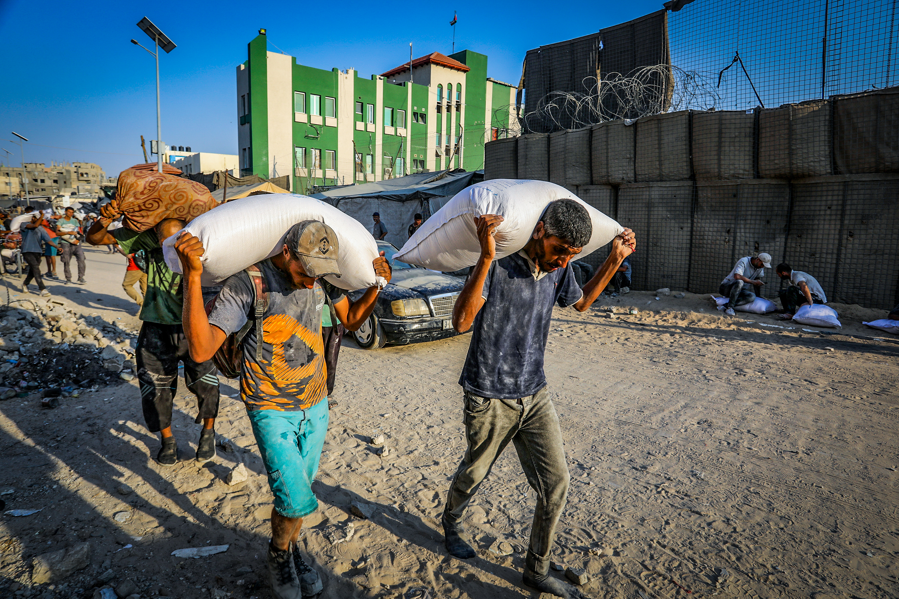 Palestinians walk through the streets with bags of flour after humanitarian aid trucks arrived via the Kerem Shalom crossing into southern Gaza, in Khan Yunis, July 24, 2025. 