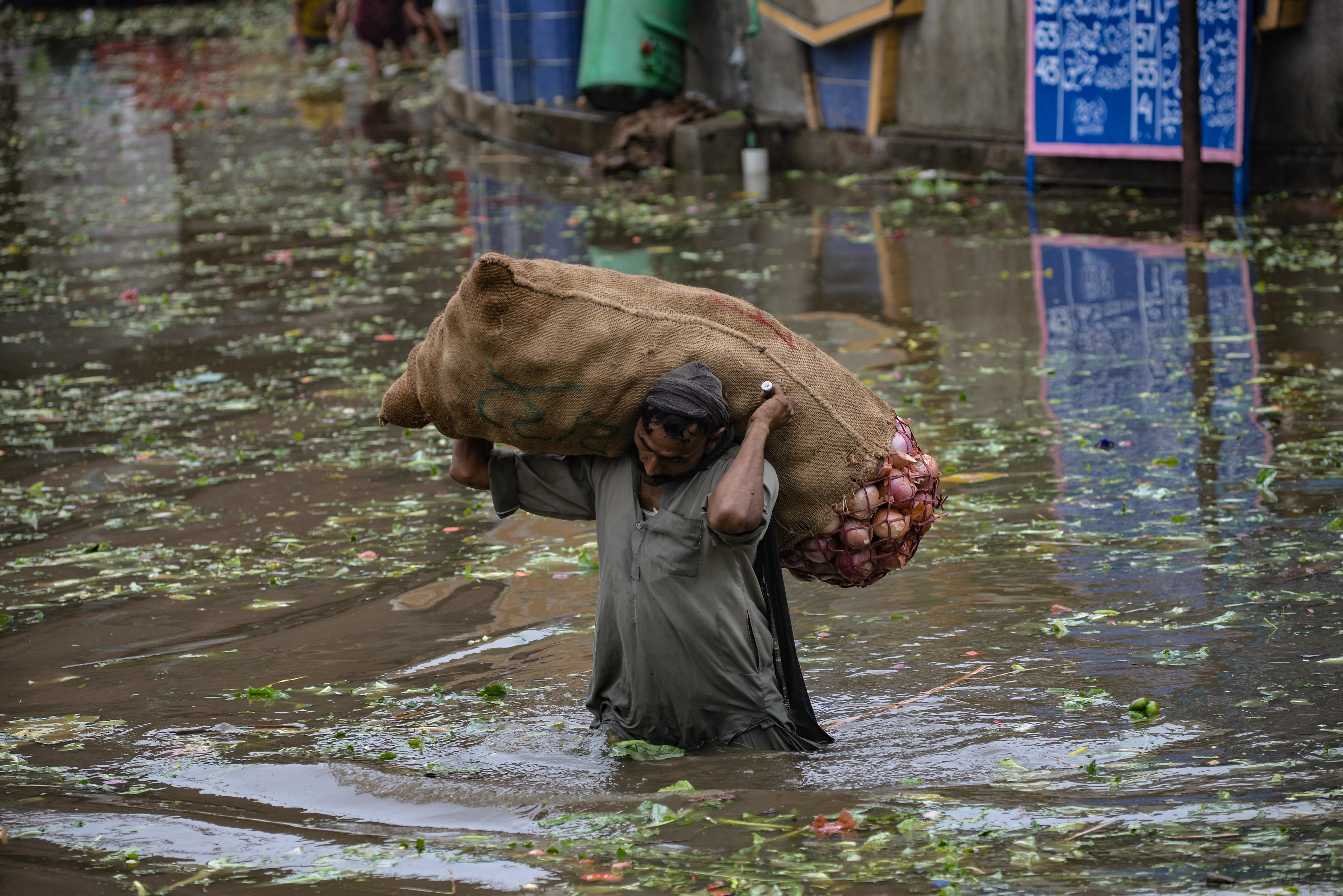 A labourer carries a basket loaded with vegetables as he wades through a flooded street after heavy monsoon rains in Lahore 