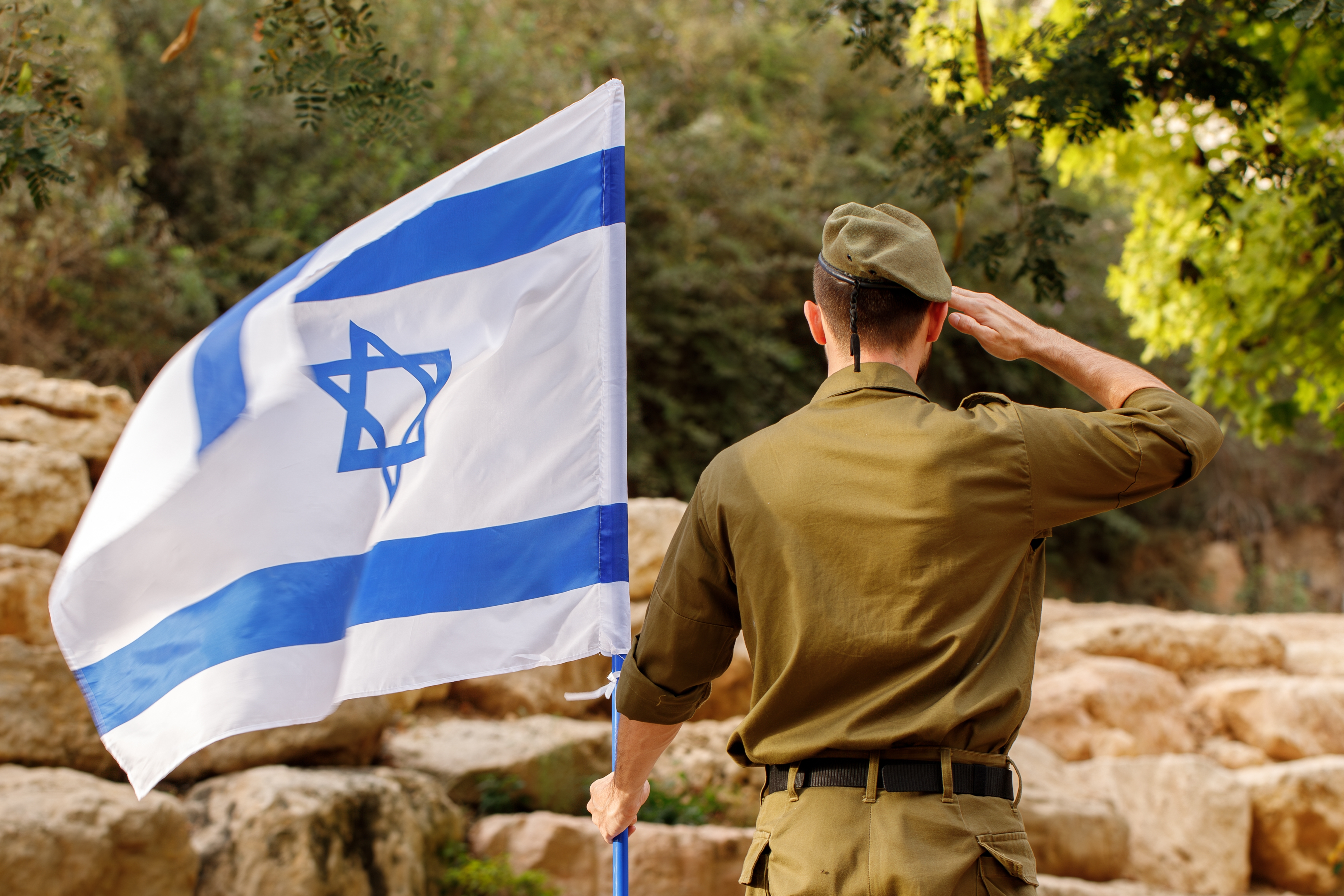 Israeli soldier stands in a field with Flag of Israel in the blooming desert