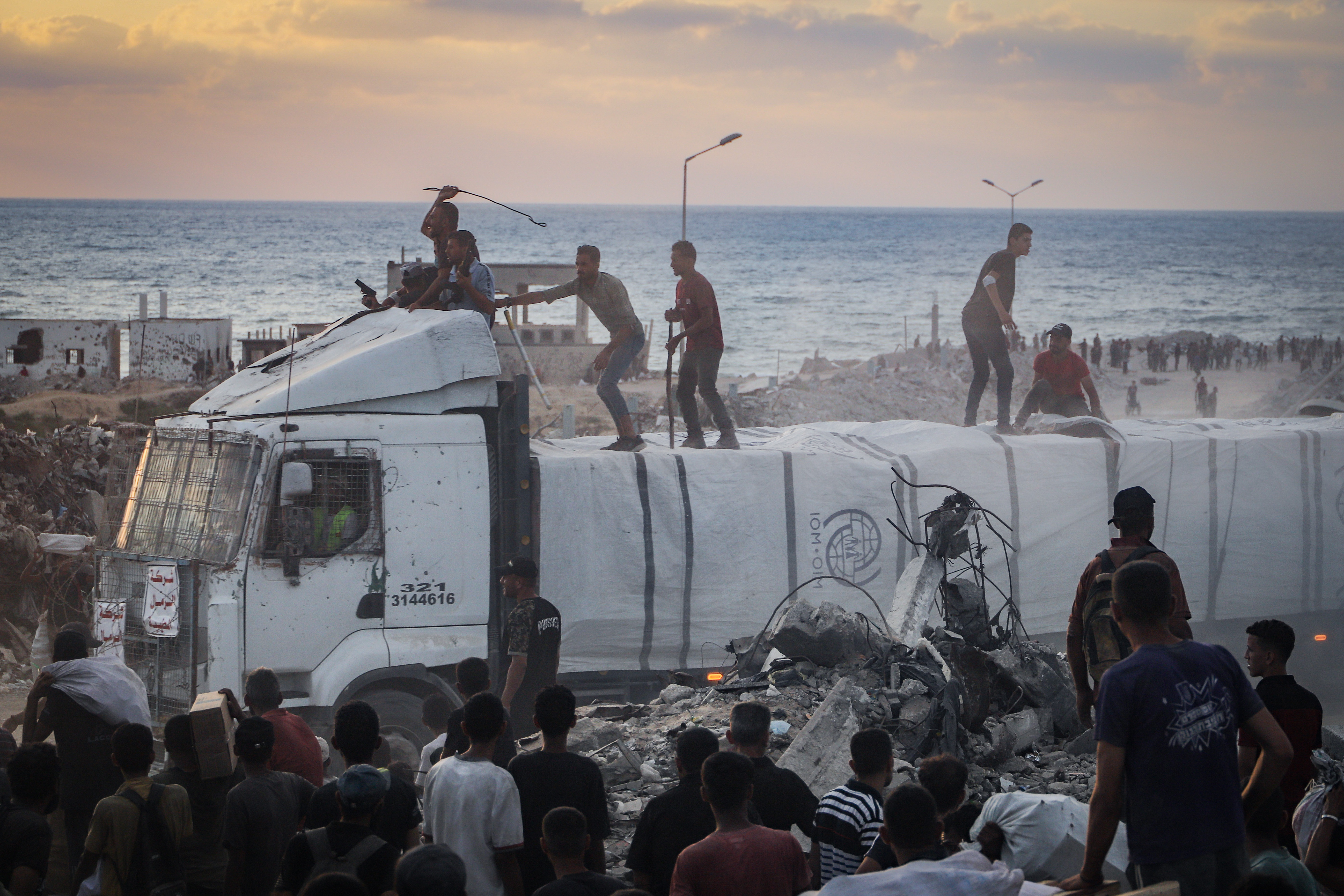 Armed Palestinians sit on trucks carrying humanitarian aid near the Zikim border crossing between Israel and Beit Lahia in the northern Gaza Strip, August 18, 2025. 