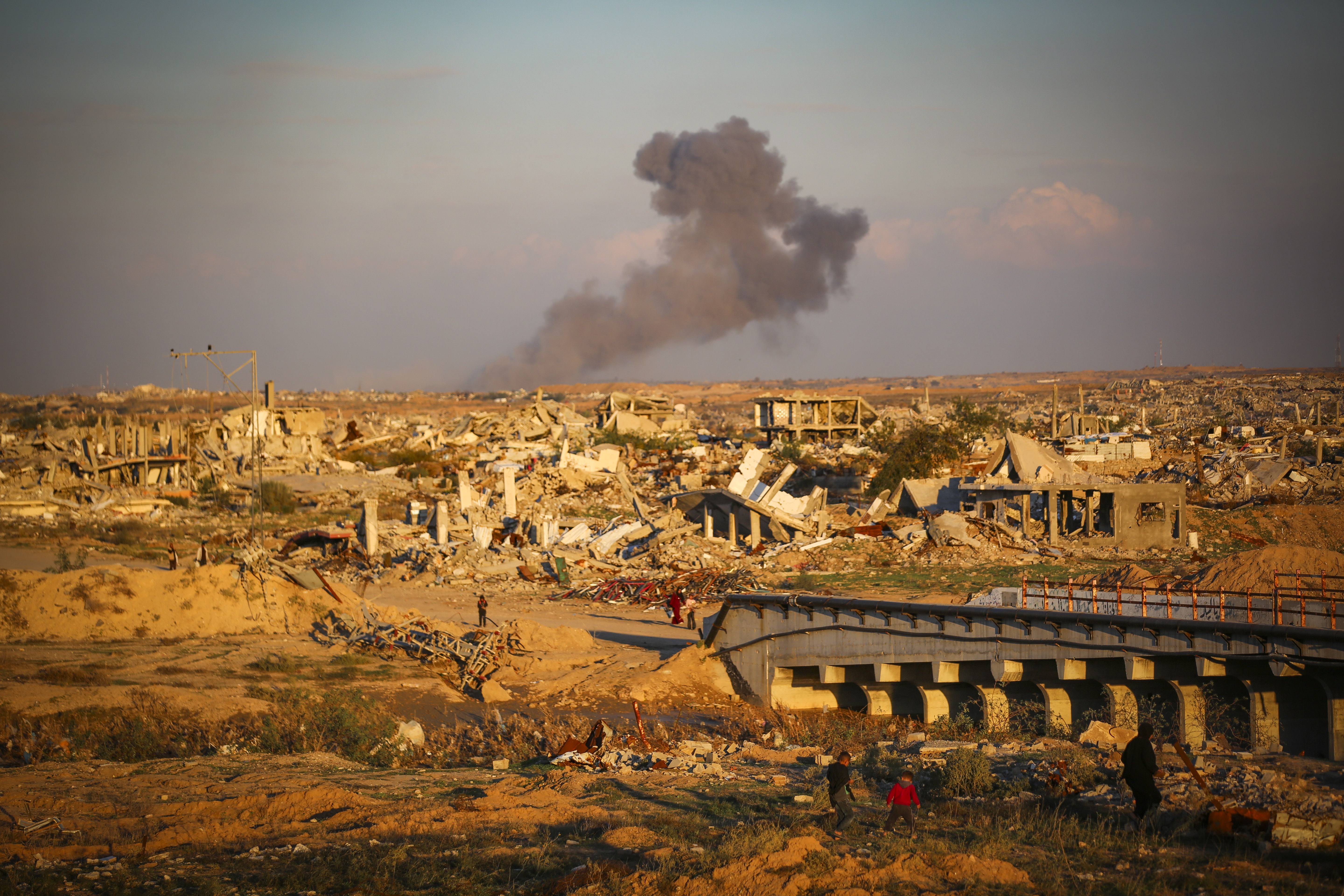 Palestinians walk in the street as smoke rises following an Israeli airstrike in Gaza City, December 2, 2025.