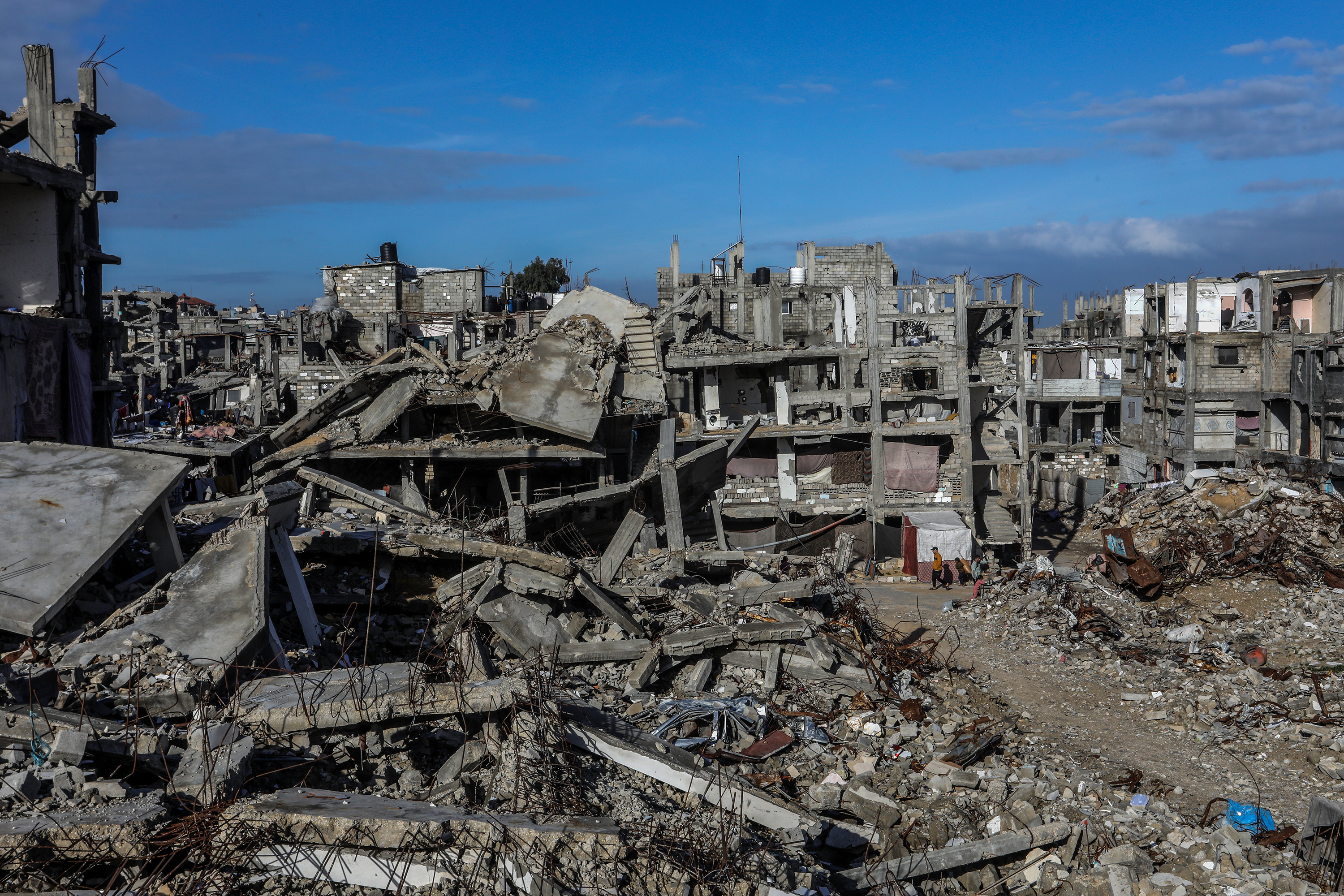 Palestinians seen near buildings destroyed in the recent war, in Khan Yunis, in the southern Gaza Strip, December 30, 2025.