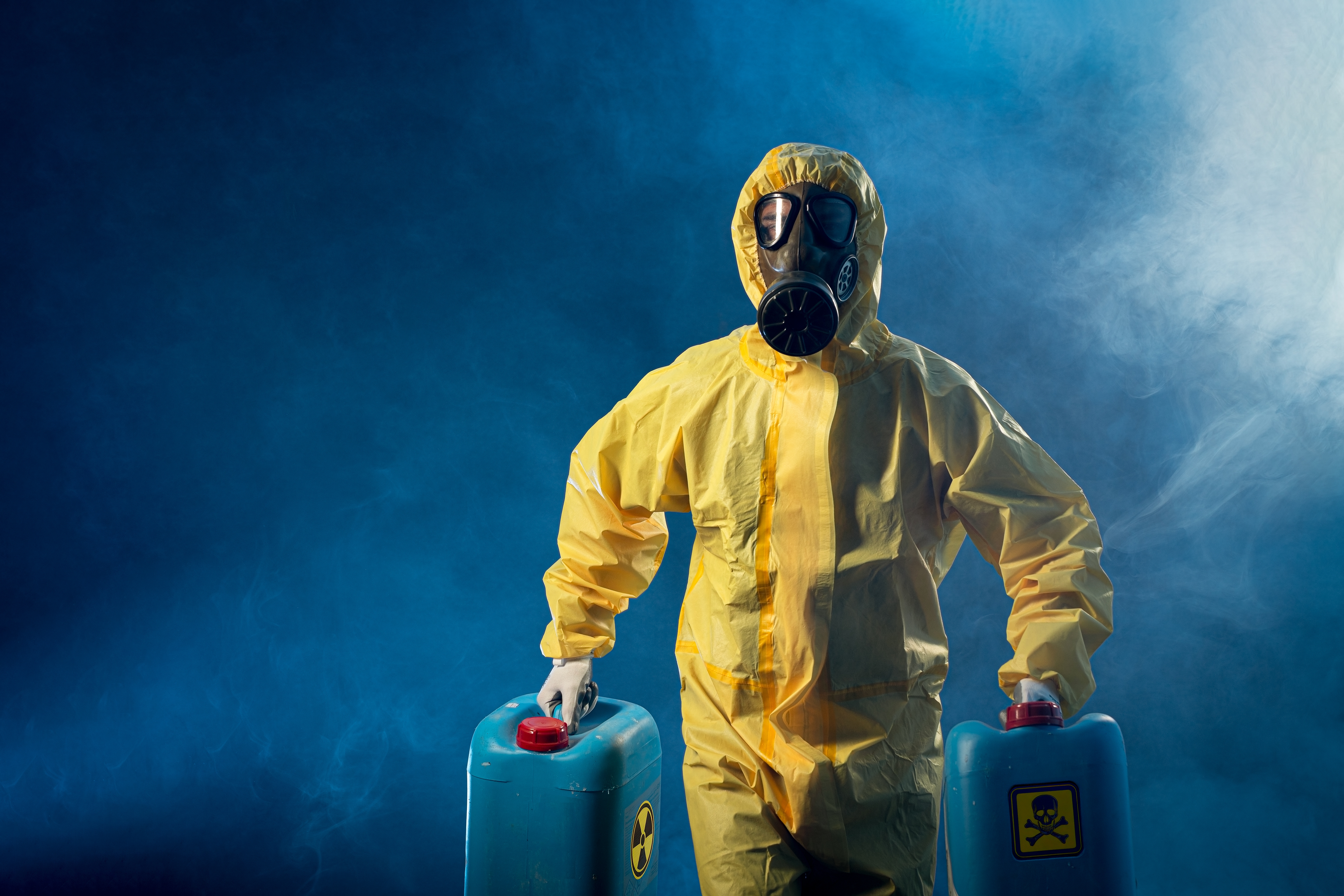 Man with safety equipment and gas mask carrying two canisters of toxic material 