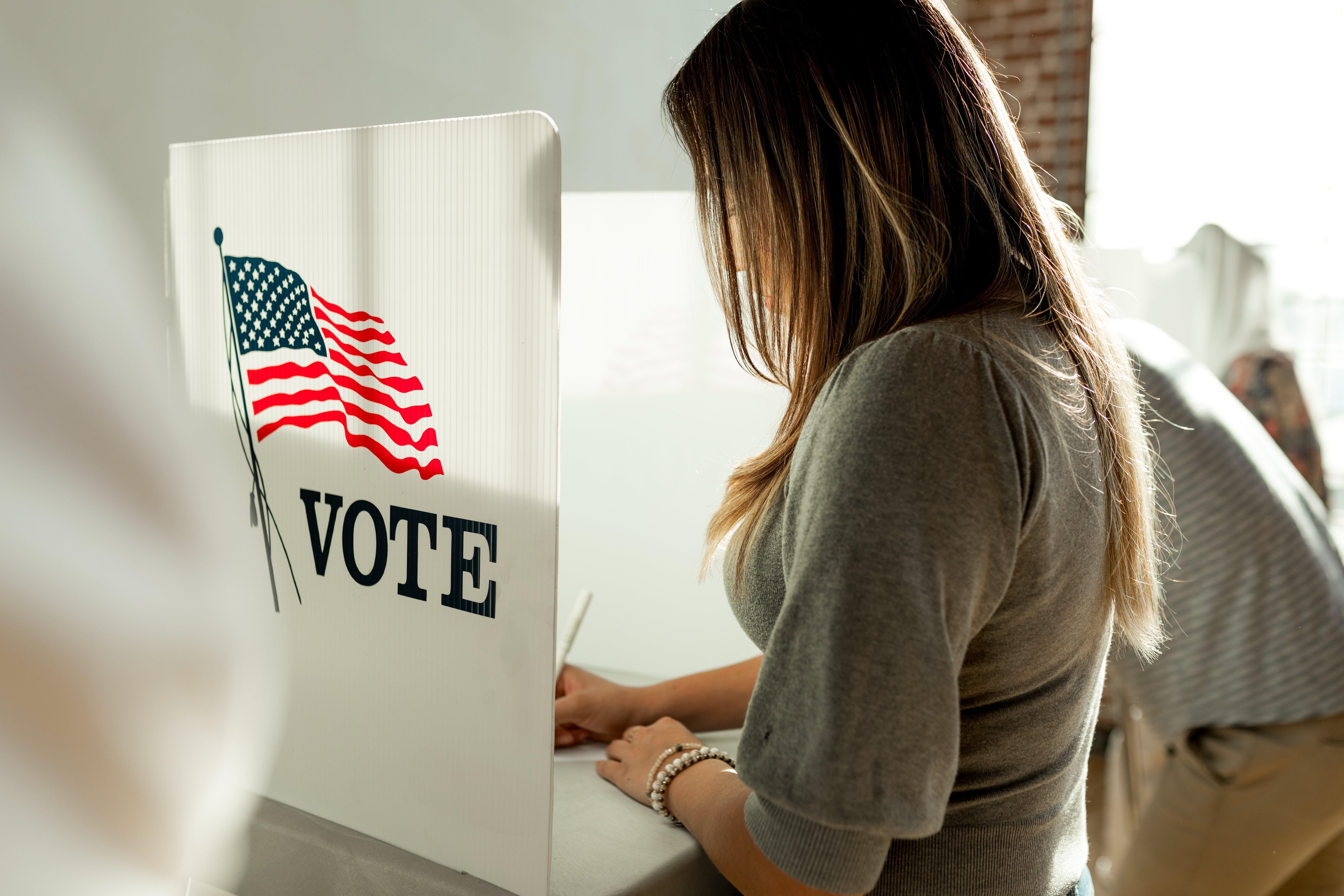 Woman voting in a booth privacy participation decision. Us election day voting booth, Voting booth with US flag. US election day. Vote for American democracy.