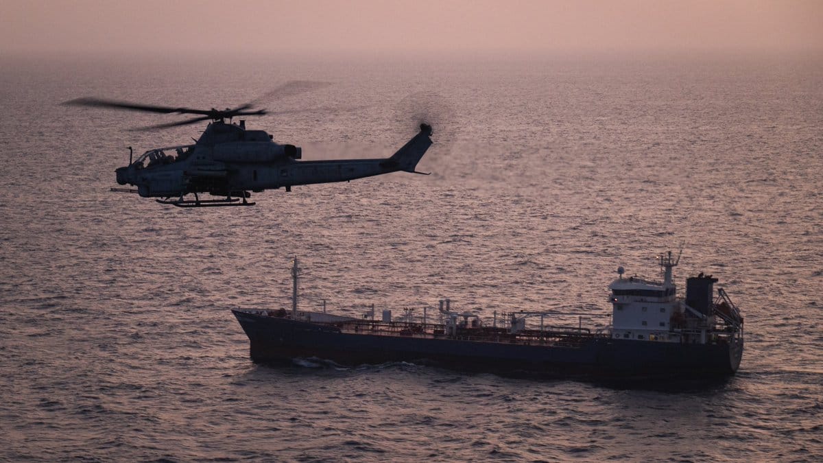 A U.S. Marine Corps AH-1Z Viper attack helicopter patrols near a commercial vessel transiting regional waters as American forces enforce the maritime blockade against I