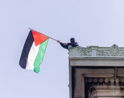 NEW YORK, N.Y. – April 30, 2024: A demonstrator waves a Palestinian flag on the roof of Hamilton Hall at Columbia University in Manhattan.