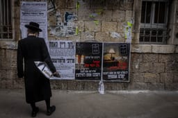 Ultra Orthodox Jews walking next to a Pashkevil on the IDF draft law in the ultra orthodox neighborhood of Mea Shearim, in Jerusalem, March 15, 2024. 