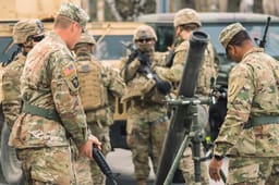 United States Marine Corps soldiers with helmets and shotguns or rifles preparing a mortar