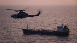 A U.S. Marine Corps AH-1Z Viper attack helicopter patrols near a commercial vessel transiting regional waters as American forces enforce the maritime blockade against I