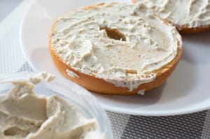 A closeup view of gluten-free bagel slices on a plate, smeared with dairy-free cream cheese