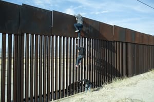 Migrants climbing a border wall.