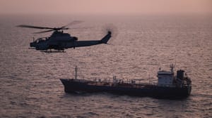 A U.S. Marine Corps AH-1Z Viper attack helicopter patrols near a commercial vessel transiting regional waters as American forces enforce the maritime blockade against I