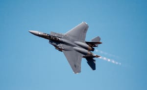 A USAF F-15E Strike Eagle fighter jet flying with afterburners in blue sky