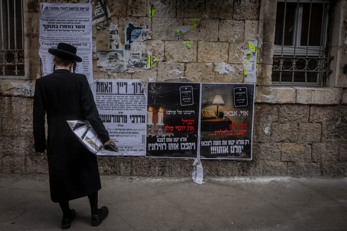 Ultra Orthodox Jews walking next to a Pashkevil on the IDF draft law in the ultra orthodox neighborhood of Mea Shearim, in Jerusalem, March 15, 2024. 