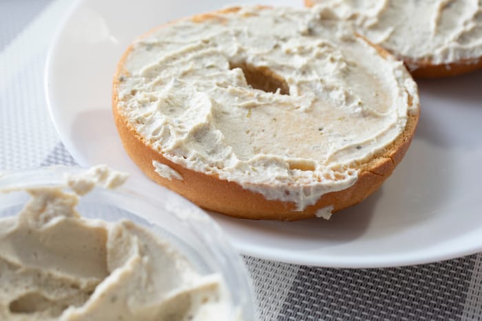 A closeup view of gluten-free bagel slices on a plate, smeared with dairy-free cream cheese
