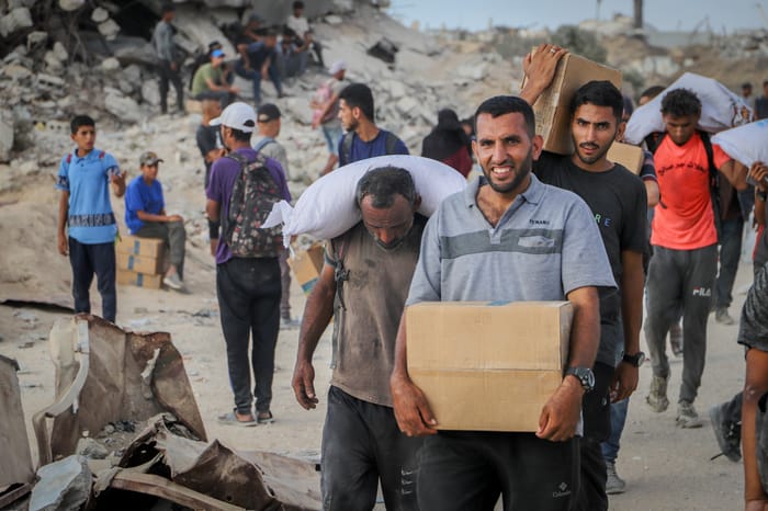 Displaced Palestinians carry food parcels and supplies from aid trucks near the Zikim border crossing between Israel and Beit Lahia, in the northern Gaza Strip, August 18, 2025.