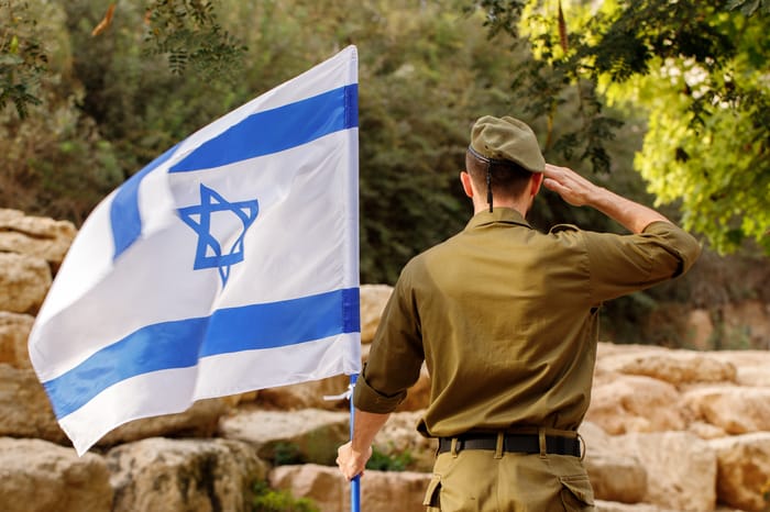 Israeli soldier stands in a field with Flag of Israel in the blooming desert