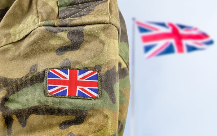 Military man posing in front of UK flag.