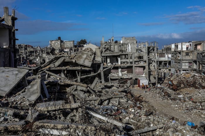 Palestinians seen near buildings destroyed in the recent war, in Khan Yunis, in the southern Gaza Strip, December 30, 2025.