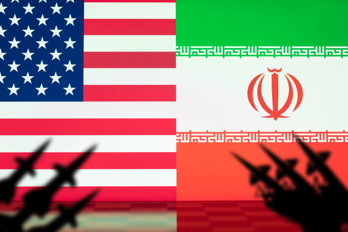Flags of the United States and Iran with missile launchers in silhouette, portraying the rising conflict and danger of war between the two nations.