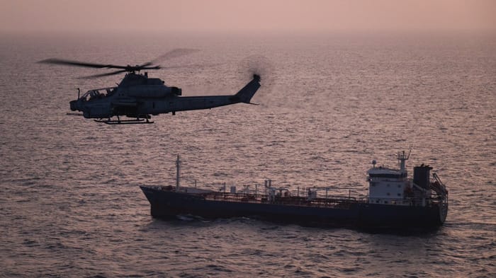 A U.S. Marine Corps AH-1Z Viper attack helicopter patrols near a commercial vessel transiting regional waters as American forces enforce the maritime blockade against I