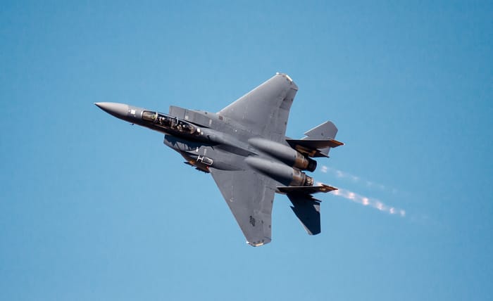A USAF F-15E Strike Eagle fighter jet flying with afterburners in blue sky
