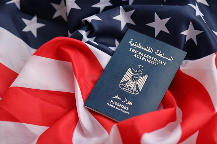 Blue Palestinian Authority passport on United States national flag background close up. Tourism and diplomacy concept