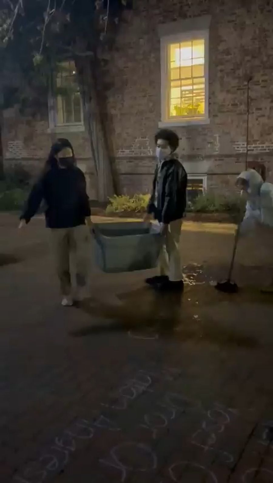 Students carrying a large bucket of water to wipe away hostage's names.
