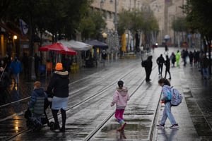 People take cover from the rain as they walk on Jaffa street in Jerusalem, December 24, 2023.