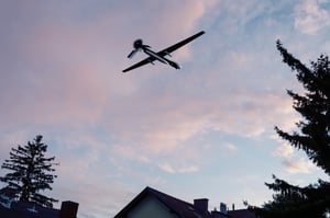 Unmanned military drone flying in the sky over residential buildings.