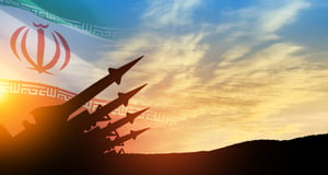 Missiles are aimed at the sky at sunset with Iran flag as the backdrop.
