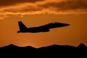 Fighter jet at sunset flying above mountains. 