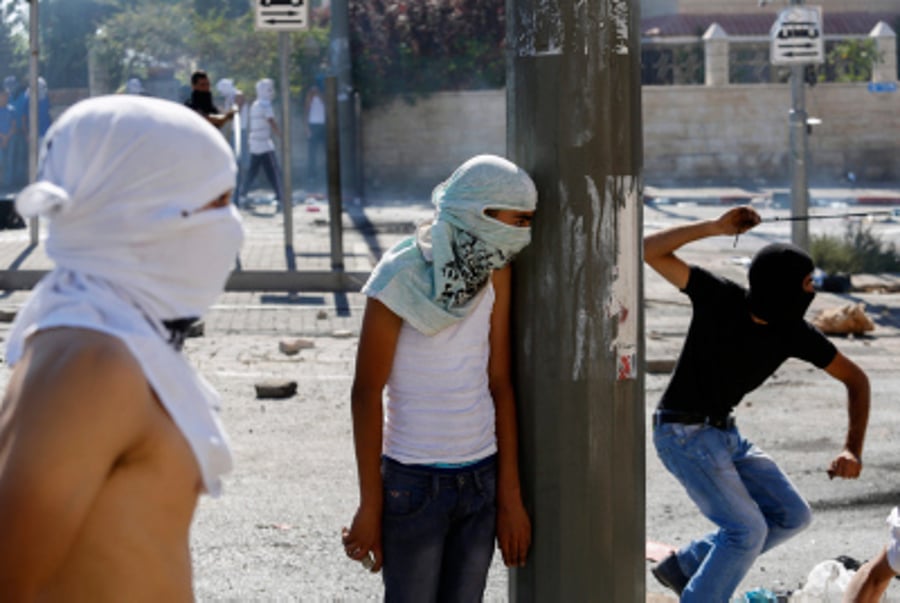 Masked Palestinian protesters throw stones towards Israeli police