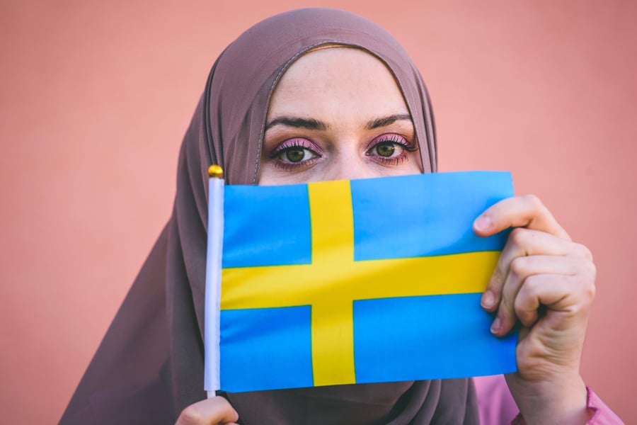 Muslim woman in a scarf holds flag of Sweden 