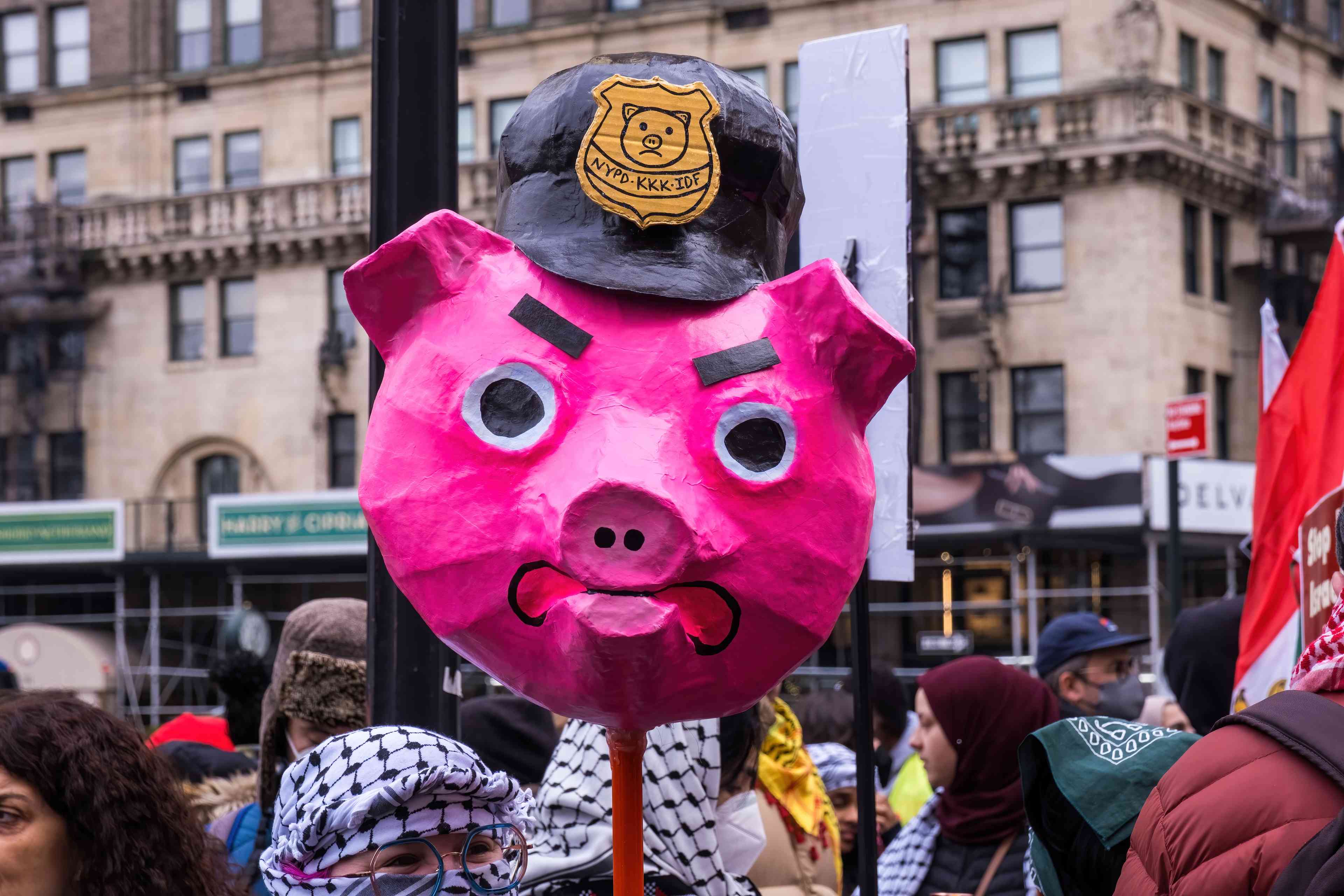 Pro-Palestine protester holds a mask of a pig whose badge says "NYPD, KKK, IDF". December, 2023. background