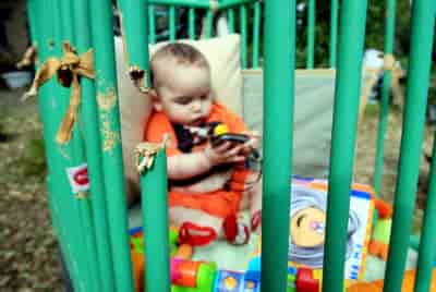 An Israeli baby is playing in his damaged bed at Kibbutz Mefalsim caused by rocket fired from the Gaza Strip background