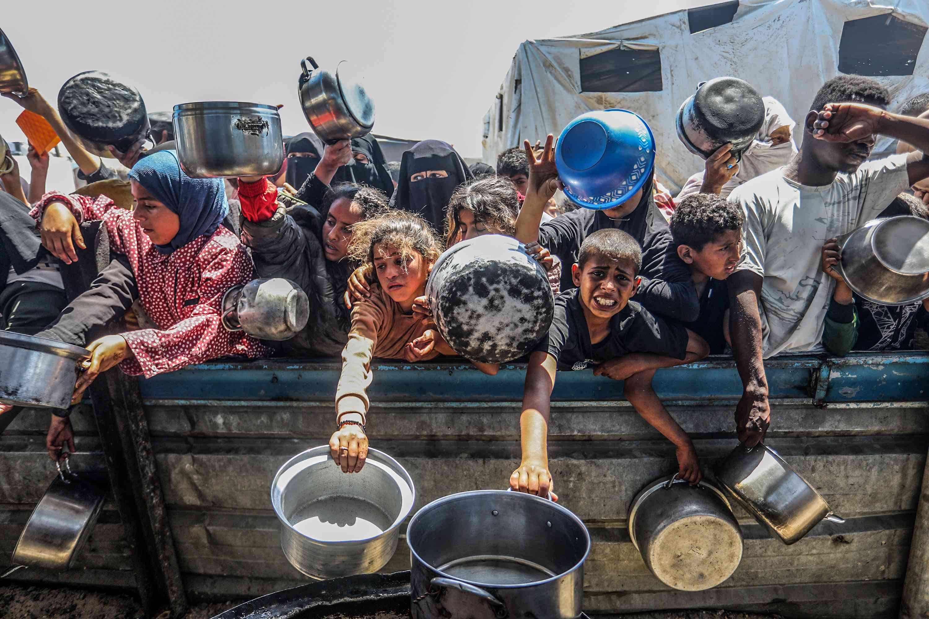 Palestinians receive meals from volunteers in the Mawasi area of ​​Khan Yunis, in the southern Gaza Strip, on April 26, 2025.  background