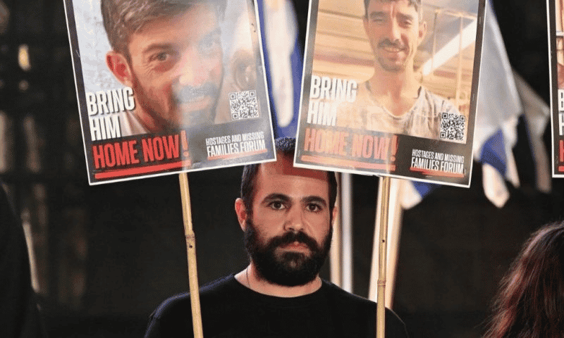 Yarden Bibas with signs of hostages David and Ariel Cunio background