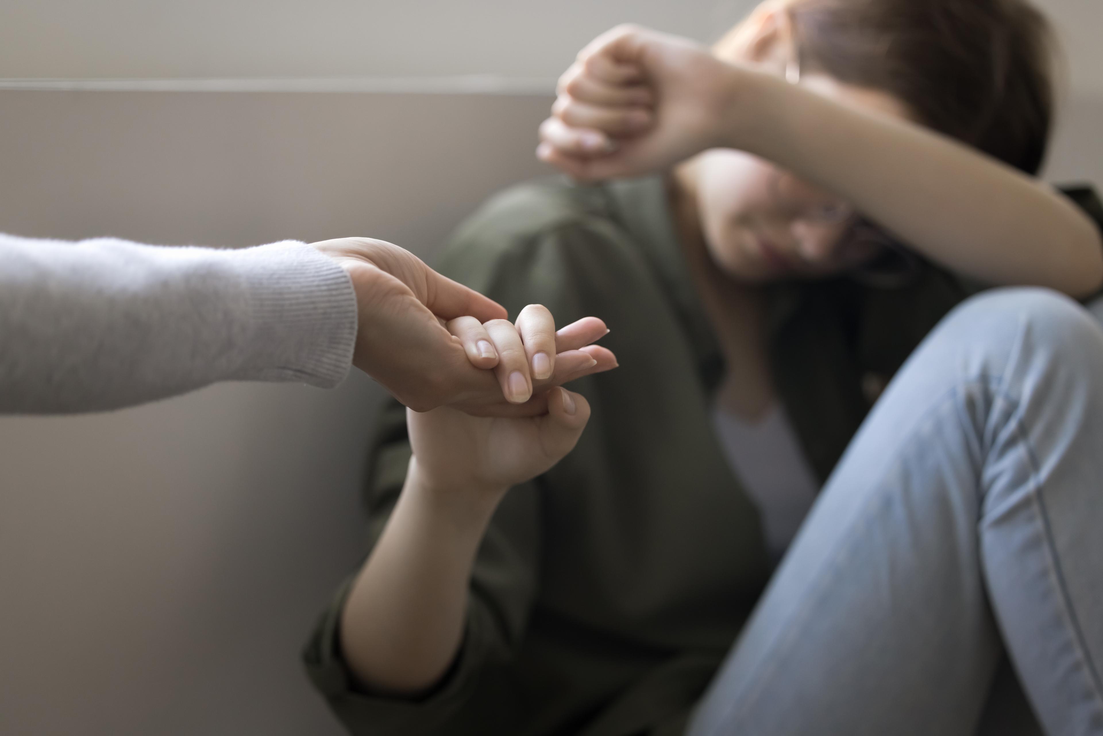 Depressed teenager kid girl taking hand of adult woman 