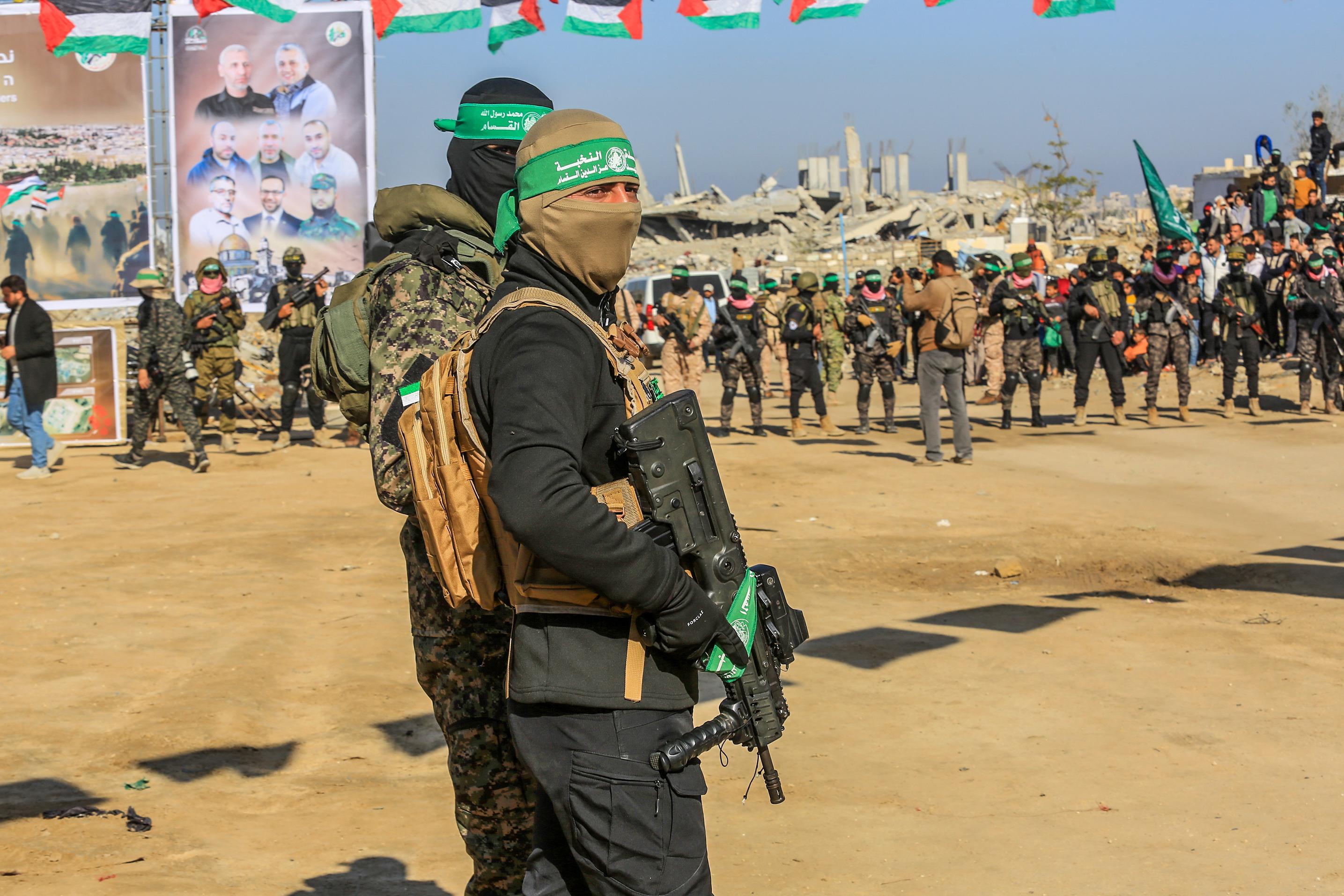 Members of the Al-Qassam Brigades guard while Palestinians watching the hand over Israeli hostages to the Red Cross, in Khan Yunis, February 15, 2025. 
