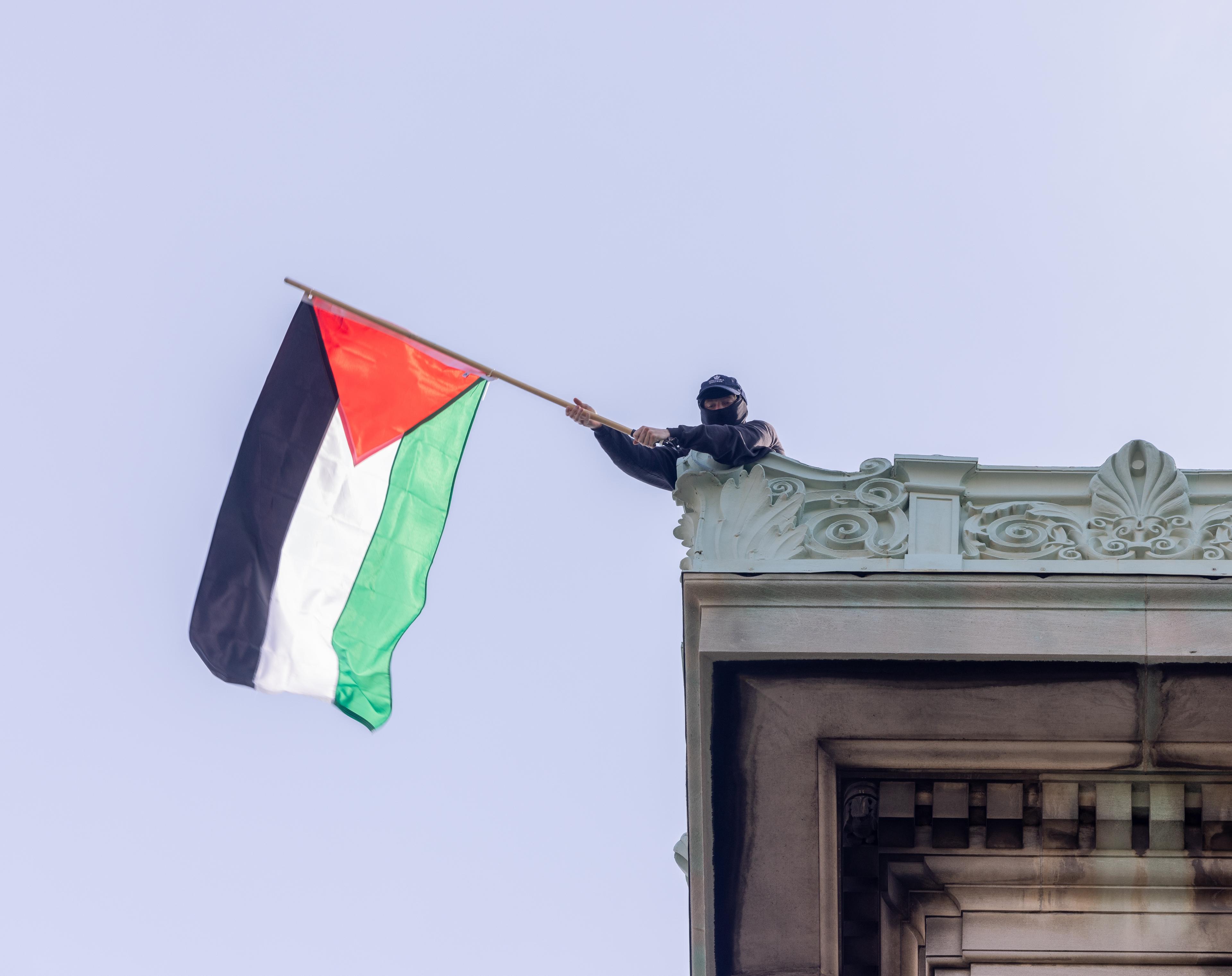 NEW YORK, N.Y. – April 30, 2024: A demonstrator waves a Palestinian flag on the roof of Hamilton Hall at Columbia University in Manhattan.
