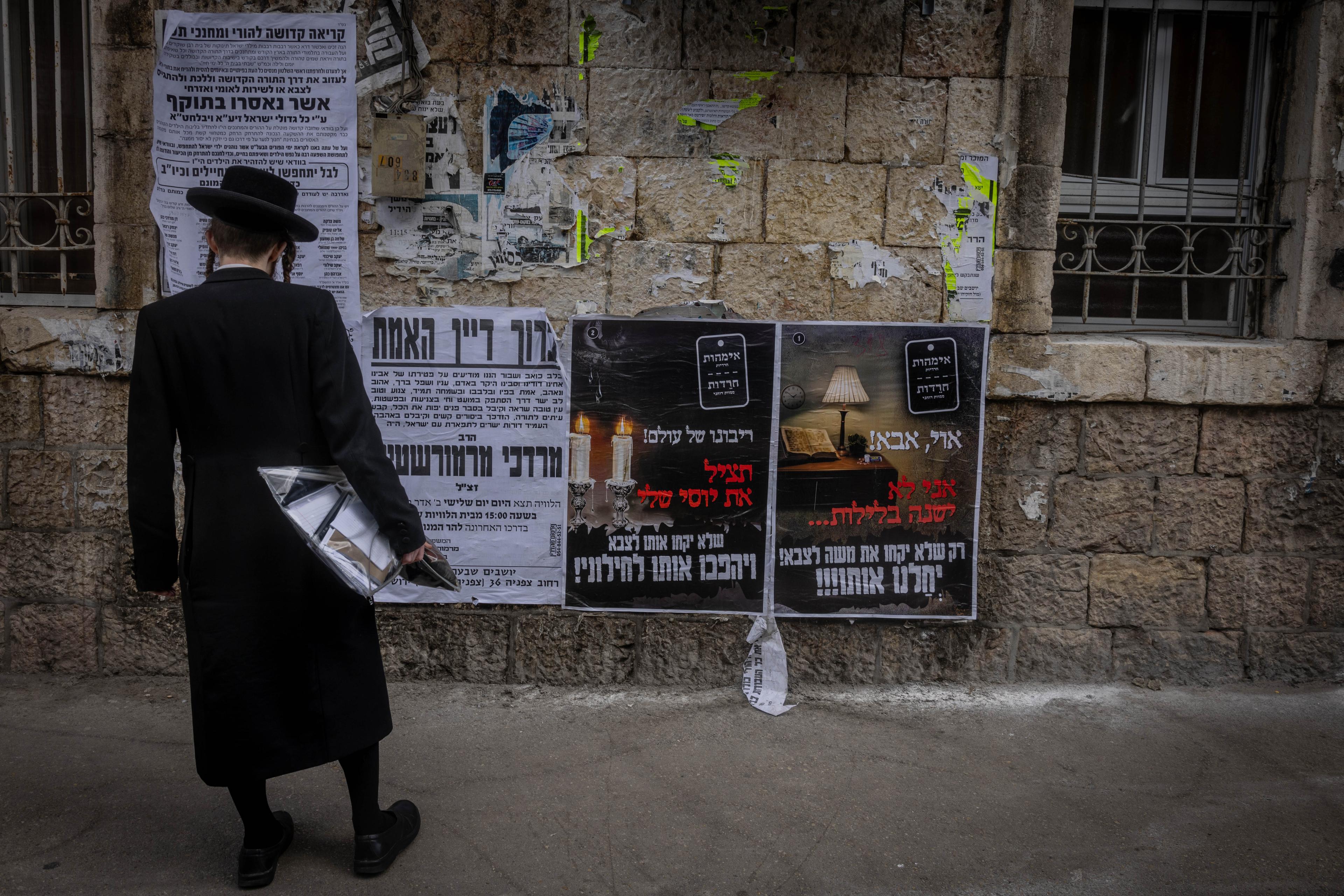 Ultra Orthodox Jews walking next to a Pashkevil on the IDF draft law in the ultra orthodox neighborhood of Mea Shearim, in Jerusalem, March 15, 2024. 