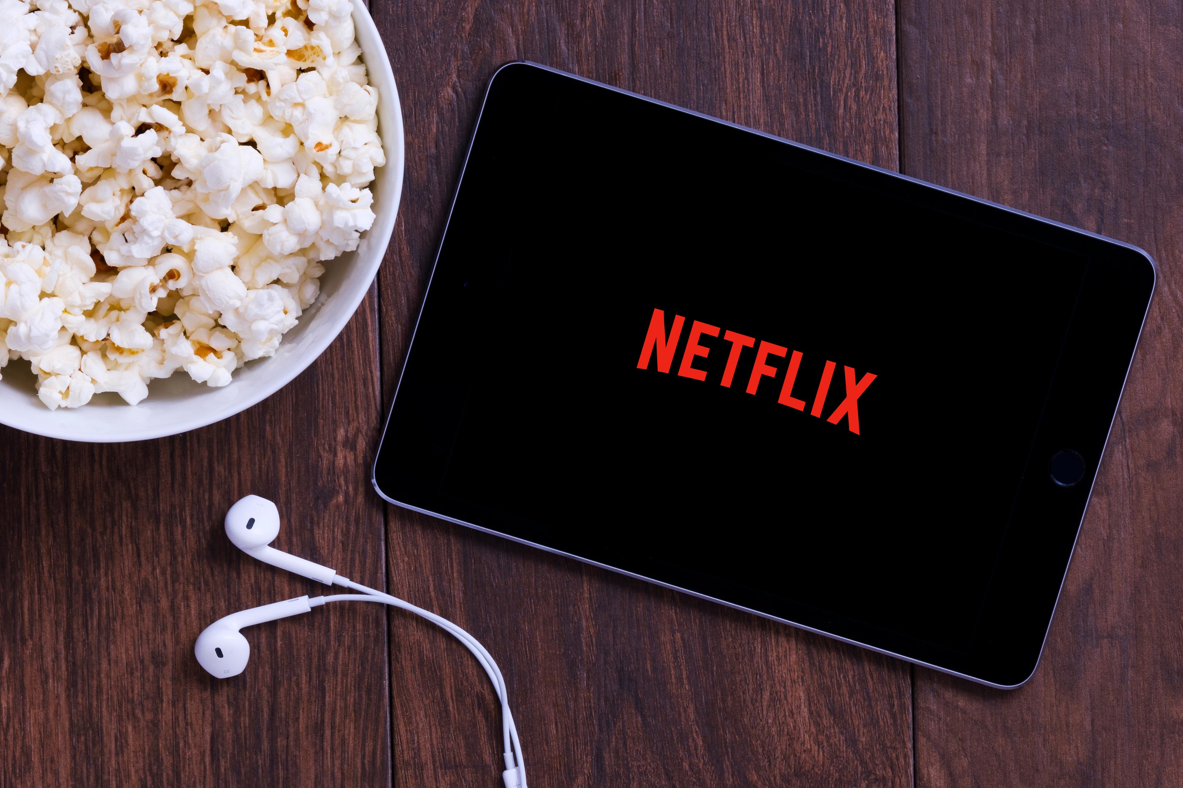  Table with popcorn and Netflix logo on Apple Ipad mini and earphones