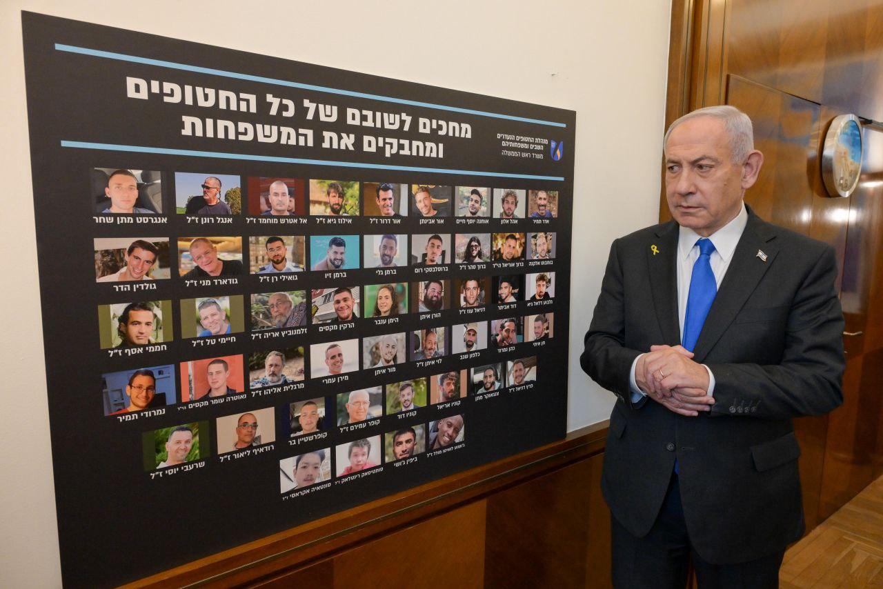Netanyahu beside a poster of the hostages still in Hamas captivity due to be released