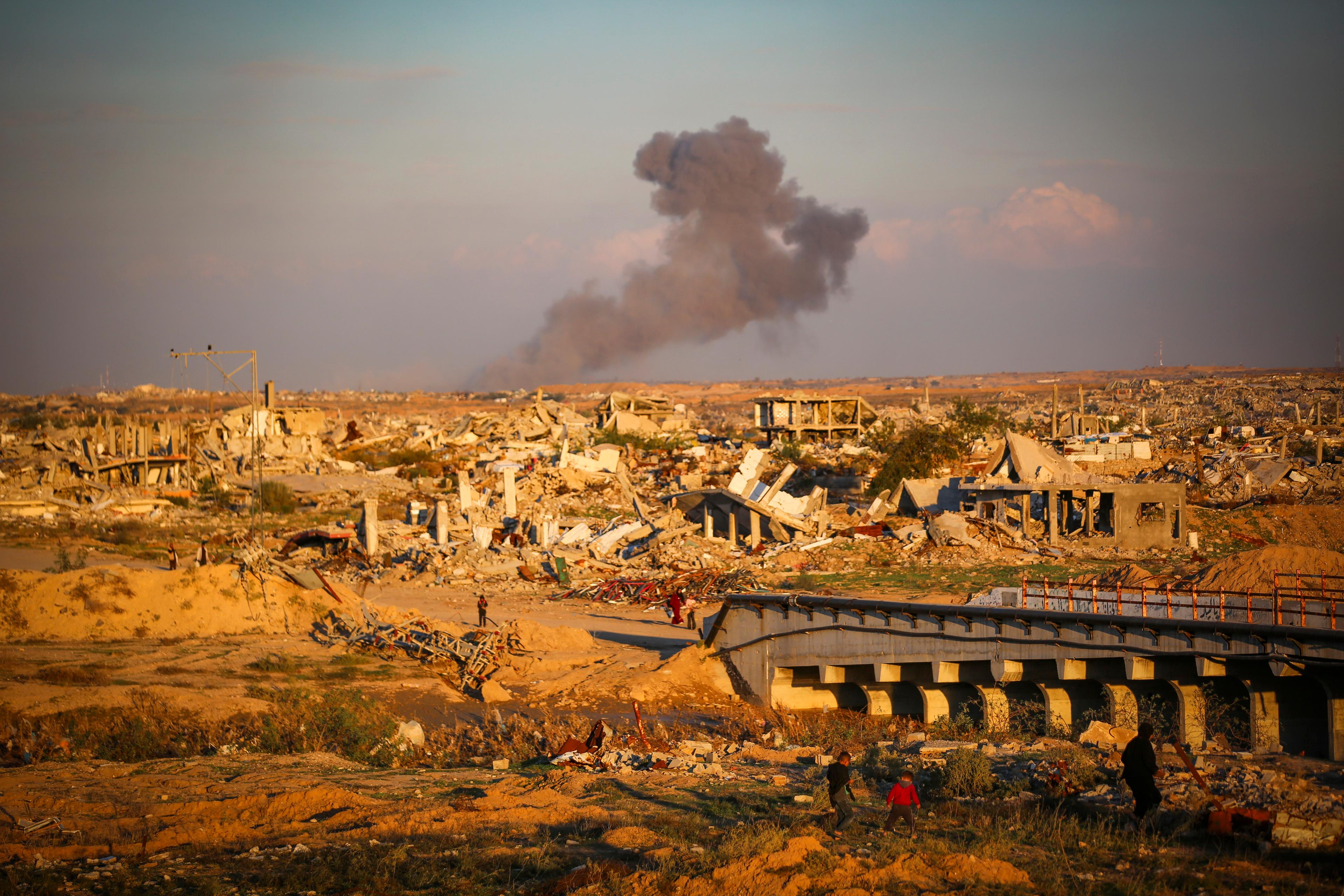 Palestinians walk in the street as smoke rises following an Israeli airstrike in Gaza City, December 2, 2025.