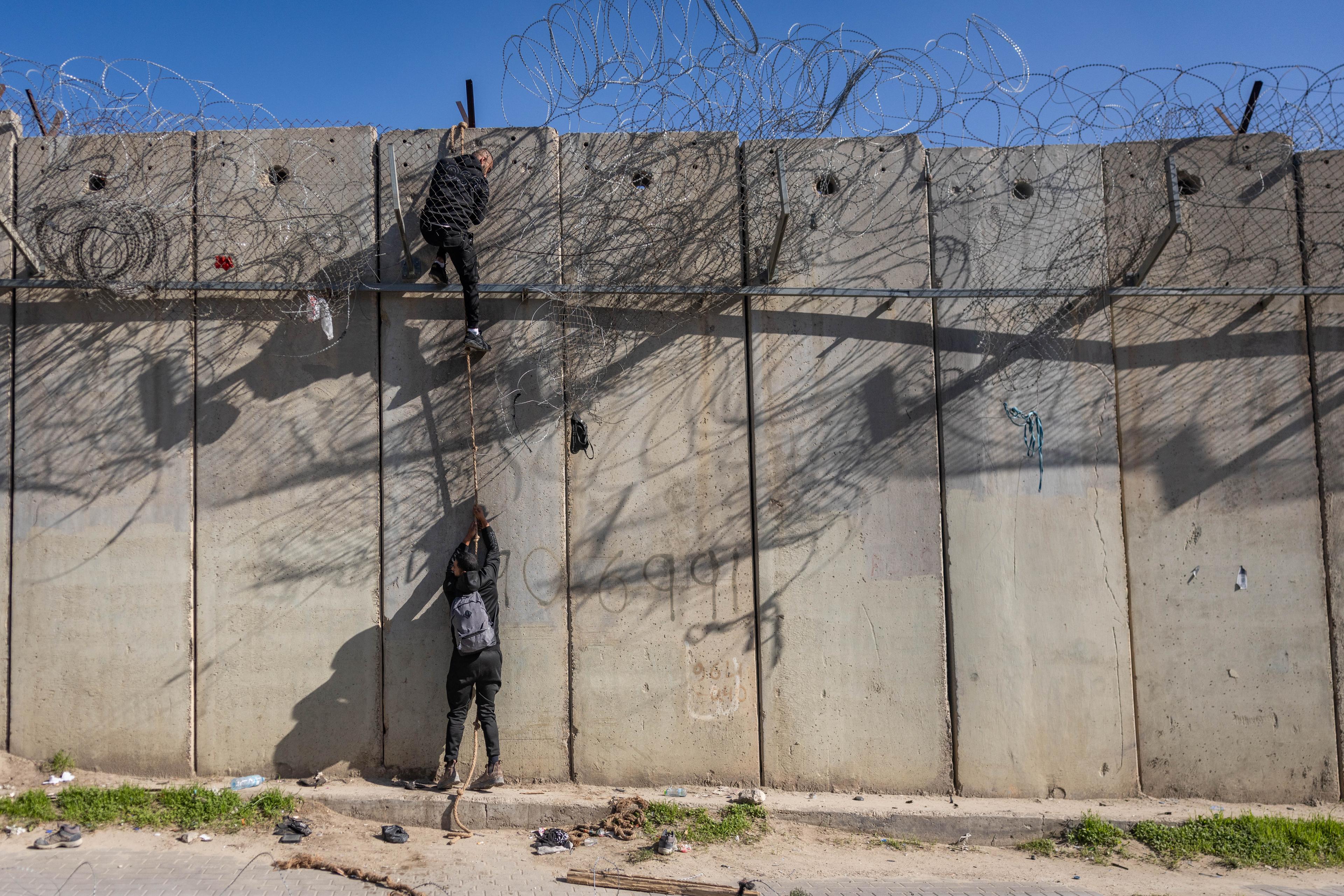 Palestinians use a rope to climb over the separation barrier from the al-Ram village into the East Jerusalem neighborhood of Beit Hanina, December 23, 2025.