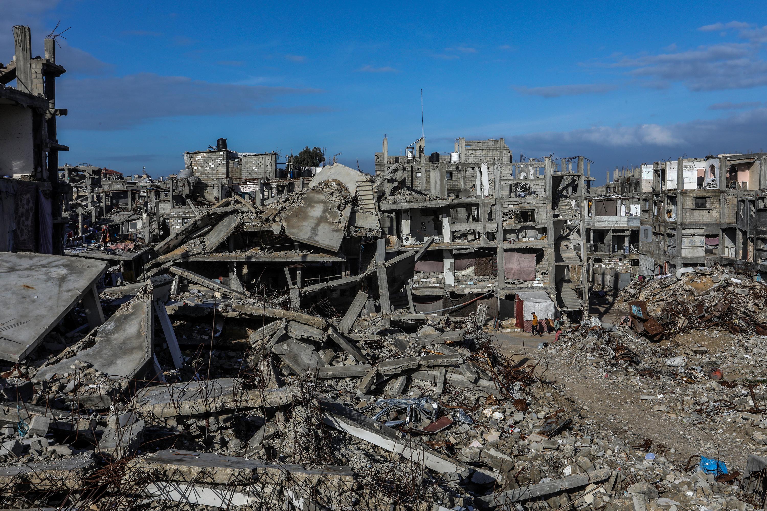 Palestinians seen near buildings destroyed in the recent war, in Khan Yunis, in the southern Gaza Strip, December 30, 2025.